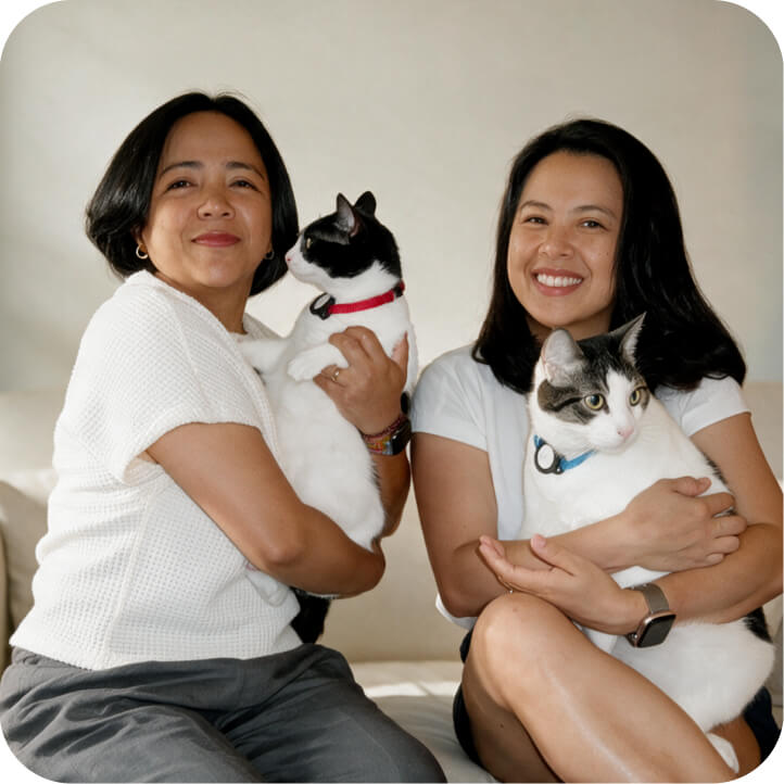 Two women smiling and holding their black and white cats